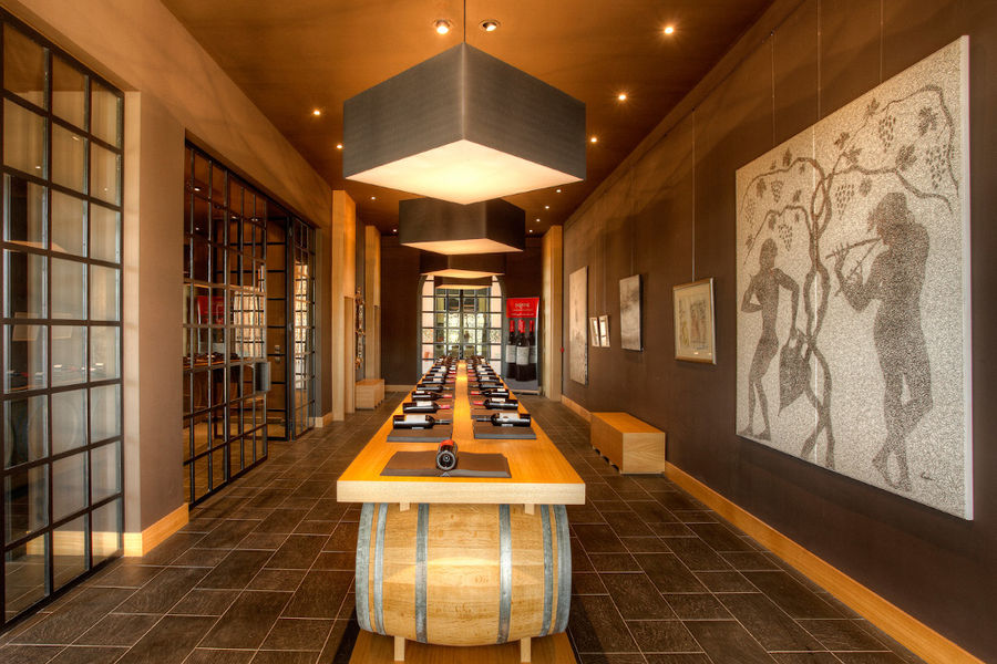 table from wood barells with wine bottles in the background of paintings on the wall of 'Domaine Skouras'